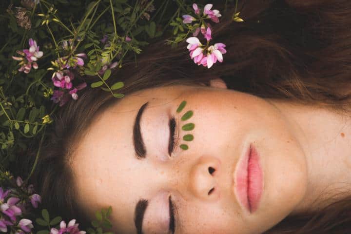 Eine Frau liegt auf der Wiese zwischen den Blumen mit geschlossenen Augen