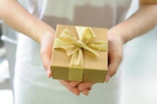 Ein Geschenkbox in Gold in der Hand von einer Dame mit dem Text " Das perfekte Geschenk"